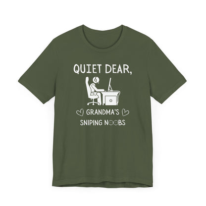 A flat image of a military green t-shirt that reads Quiet Dear, Grandma's Sniping Noobs in white text. The lower text is framed by two hearts, and the O's are in the shape of sniper scopes. In the center of the shirt is an image of a person at a desk with a gaming PC.
