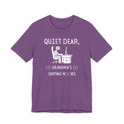 A flat image of a purple heather t-shirt that reads Quiet Dear, Grandma's Sniping Noobs in white text. The lower text is framed by two hearts, and the O's are in the shape of sniper scopes. In the center of the shirt is an image of a person at a desk with a gaming PC.