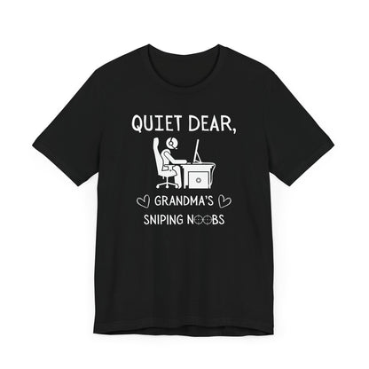 A flat image of a black t-shirt that reads Quiet Dear, Grandma's Sniping Noobs in white text. The lower text is framed by two hearts, and the O's are in the shape of sniper scopes. In the center of the shirt is an image of a person at a desk with a gaming PC.