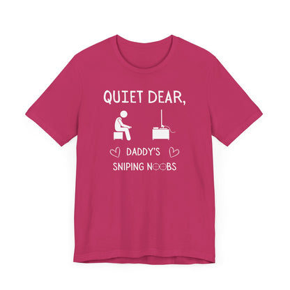 A flat image of a berry pink t-shirt that reads Quiet Dear, Daddy's Sniping Noobs in white text. The lower text is framed by two hearts, and the O's are in the shape of sniper scopes. In the center of the shirt is an image of a person holding a controller sitting across from a TV.