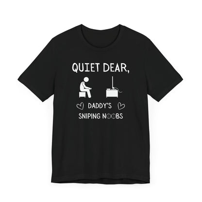 A flat image of a black t-shirt that reads Quiet Dear, Daddy's Sniping Noobs in white text. The lower text is framed by two hearts, and the O's are in the shape of sniper scopes. In the center of the shirt is an image of a person holding a controller sitting across from a TV.