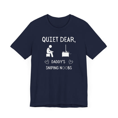 A flat image of a navy t-shirt that reads Quiet Dear, Daddy's Sniping Noobs in white text. The lower text is framed by two hearts, and the O's are in the shape of sniper scopes. In the center of the shirt is an image of a person holding a controller sitting across from a TV.