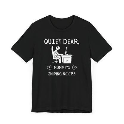 A flat image of a black t-shirt that reads Quiet Dear, Mommy's Sniping Noobs in white text. The lower text is framed by two hearts, and the O's are in the shape of sniper scopes. In the center of the shirt is an image of a person at a desk with a gaming PC.