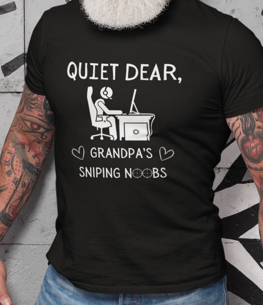 A model wearing a black t-shirt that reads Quiet Dear, Grandpa's Sniping Noobs in white text. The lower text is framed by two hearts, and the O's are in the shape of sniper scopes. In the center of the shirt is an image of a person at a desk with a gaming PC.