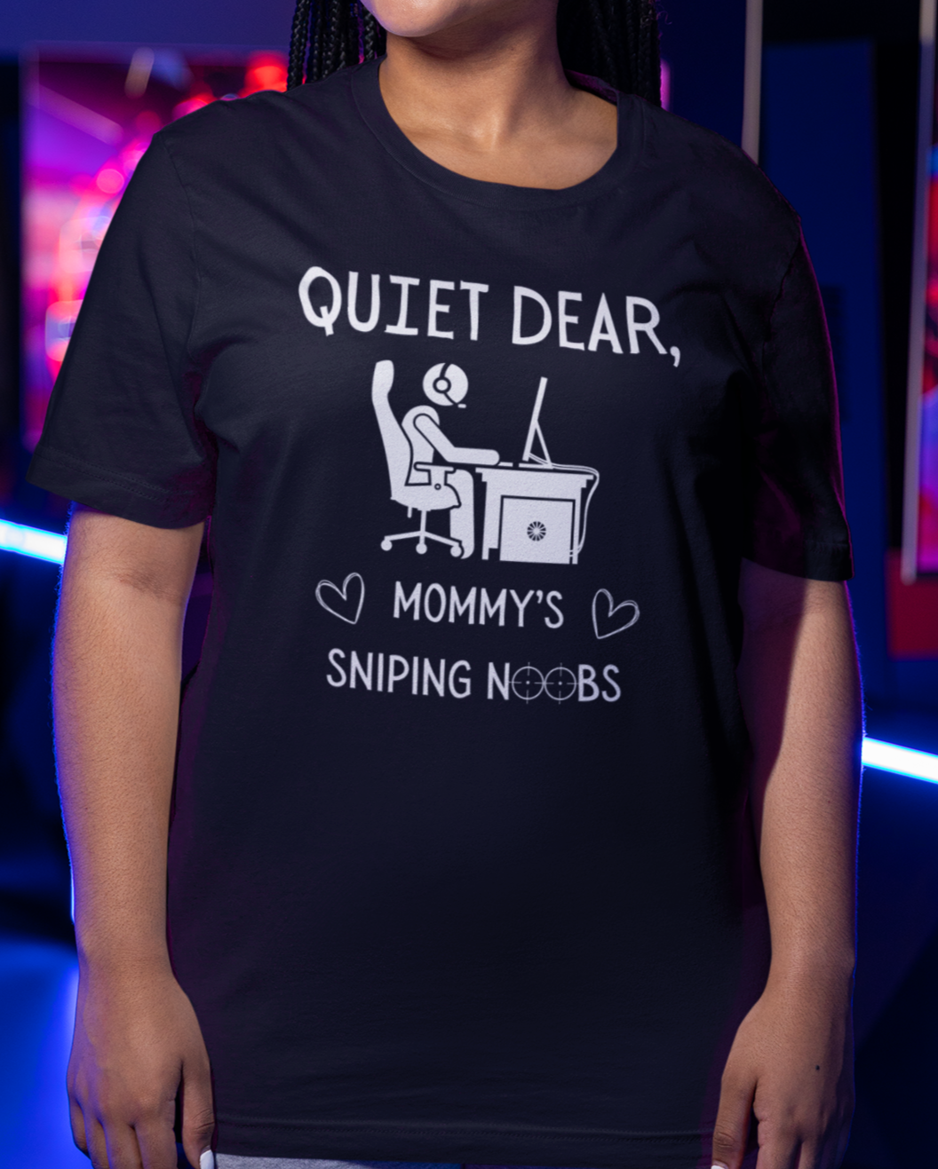 A model wearing a black t-shirt that reads Quiet Dear, Mommy's Sniping Noobs in white text. The lower text is framed by two hearts, and the O's are in the shape of sniper scopes. In the center of the shirt is an image of a person at a desk with a gaming PC.